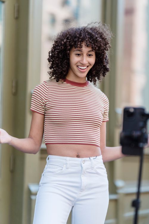 Free Positive ethnic female in stylish outfit recording live broadcast on smartphone while standing on street with buildings on blurred background Stock Photo