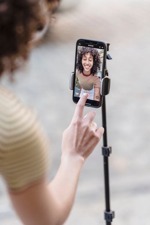 Free Crop positive ethnic female touching screen of smartphone while recording live video on street with paved sidewalk on blurred background Stock Photo