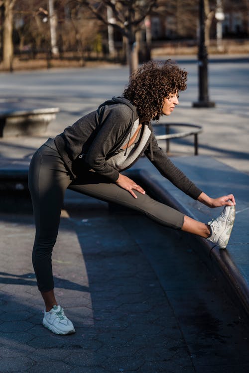 Sporty ethnic woman stretching legs on street
