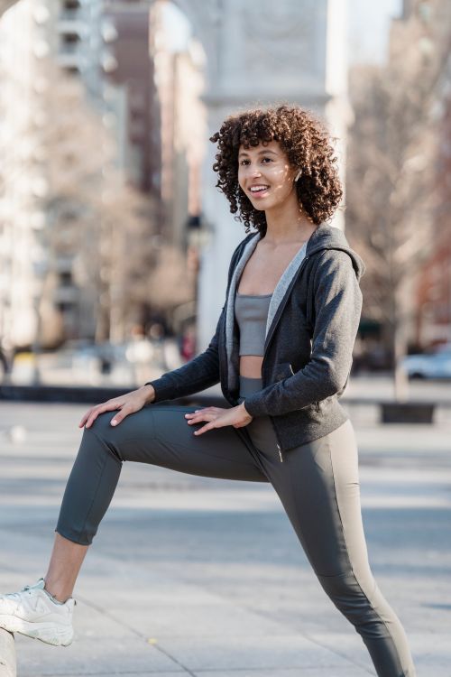Free Happy ethnic female in activewear doing warm up exercise on sunny street with residential building on blurred background in city Stock Photo