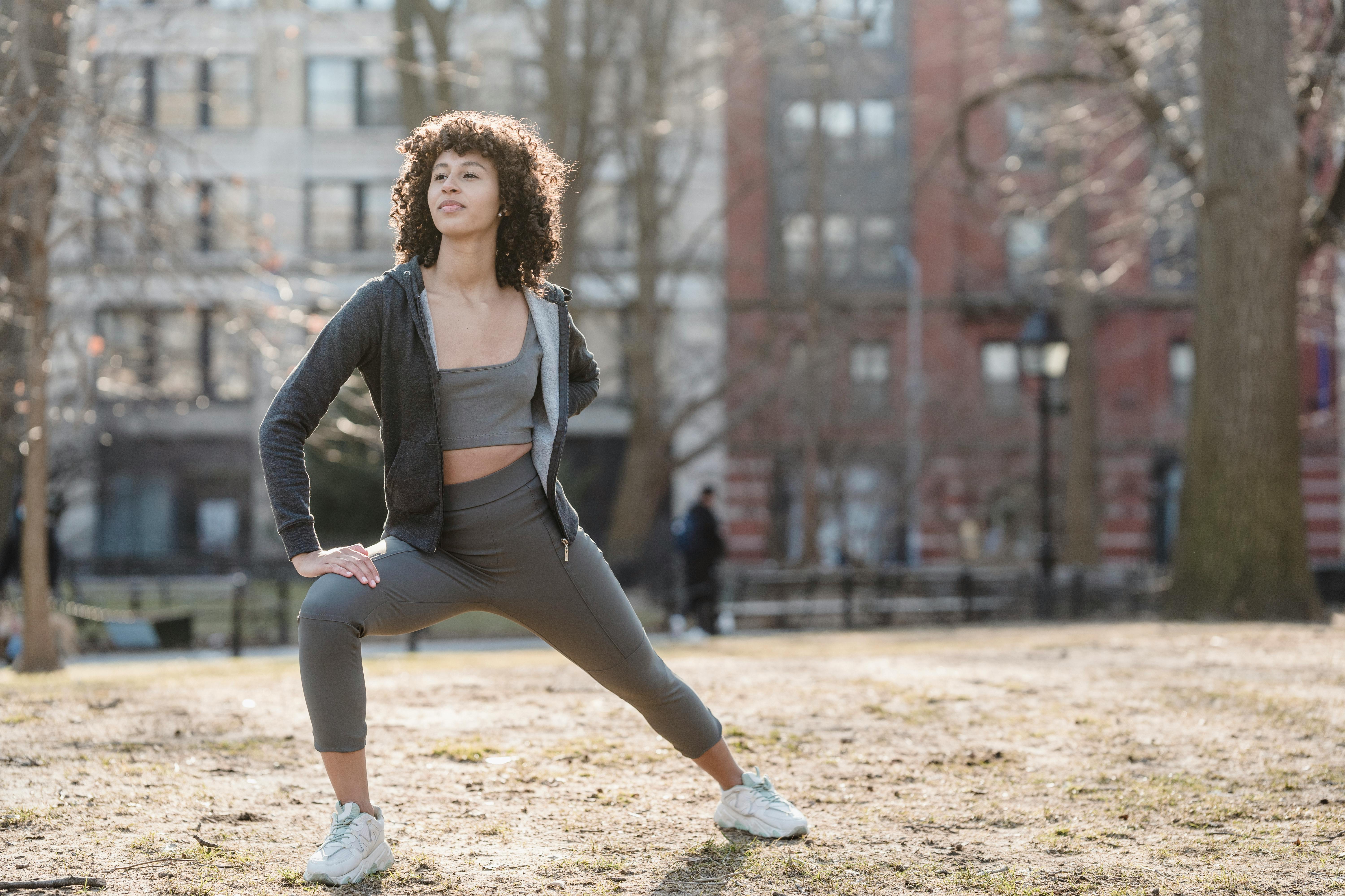 Free Full body of black female in sportswear stretching legs during fitness workout in park on blurred background and looking away Stock Photo