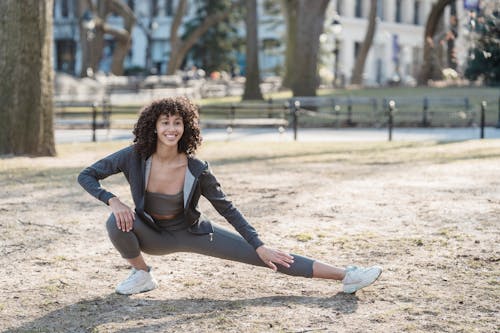 Free Flexible African American woman smiling and stretching legs in park Stock Photo