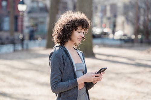 Free Black woman using smartphone for sms in park Stock Photo