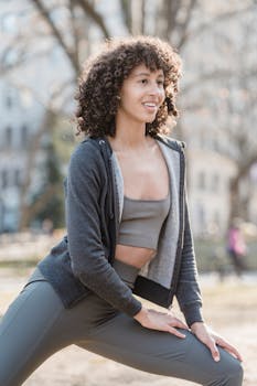 African American female in sportswear looking away and smiling while stretching legs outdoors on sunny day