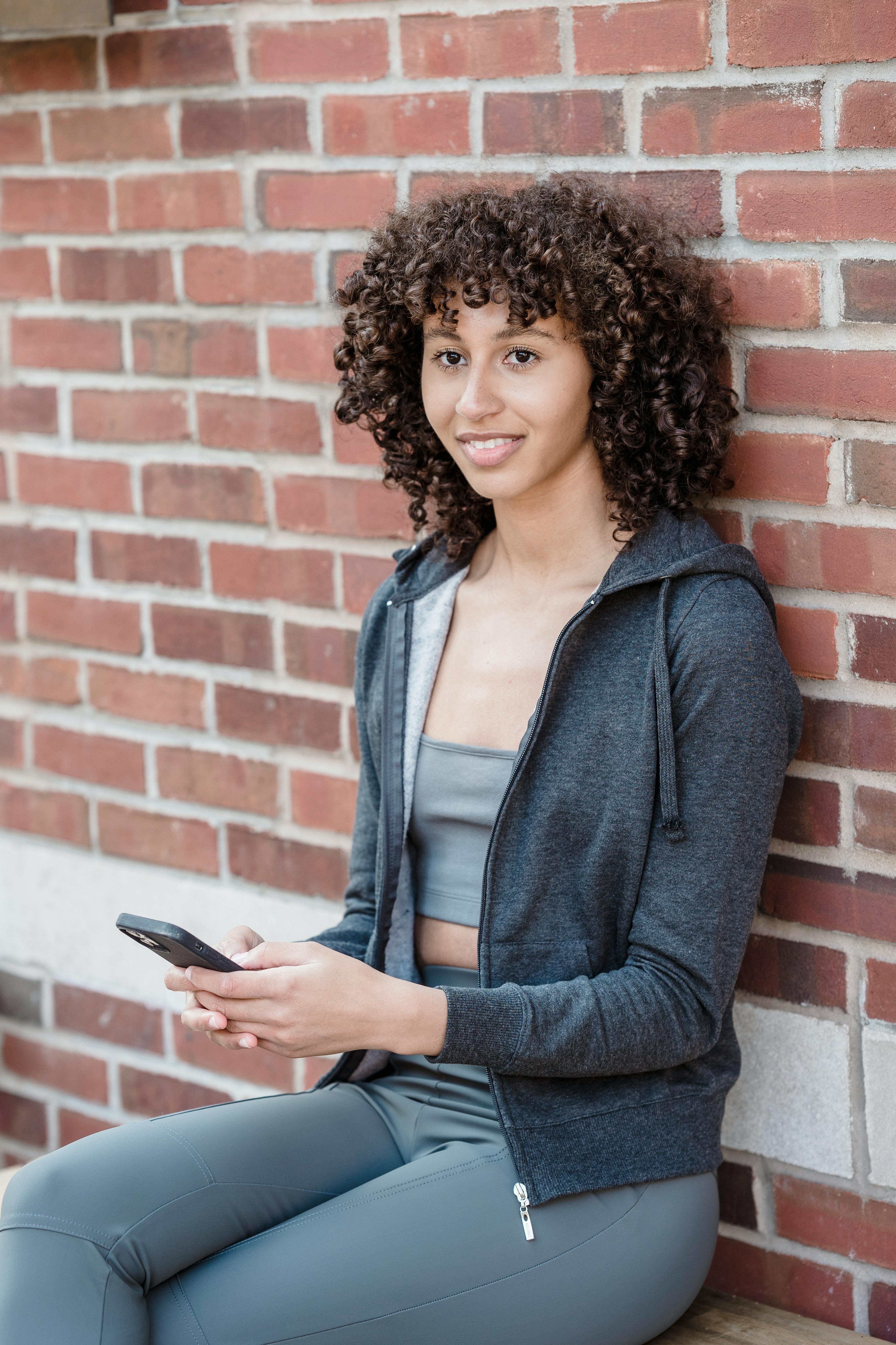 smiling young ethnic lady surfing smartphone on bench on street