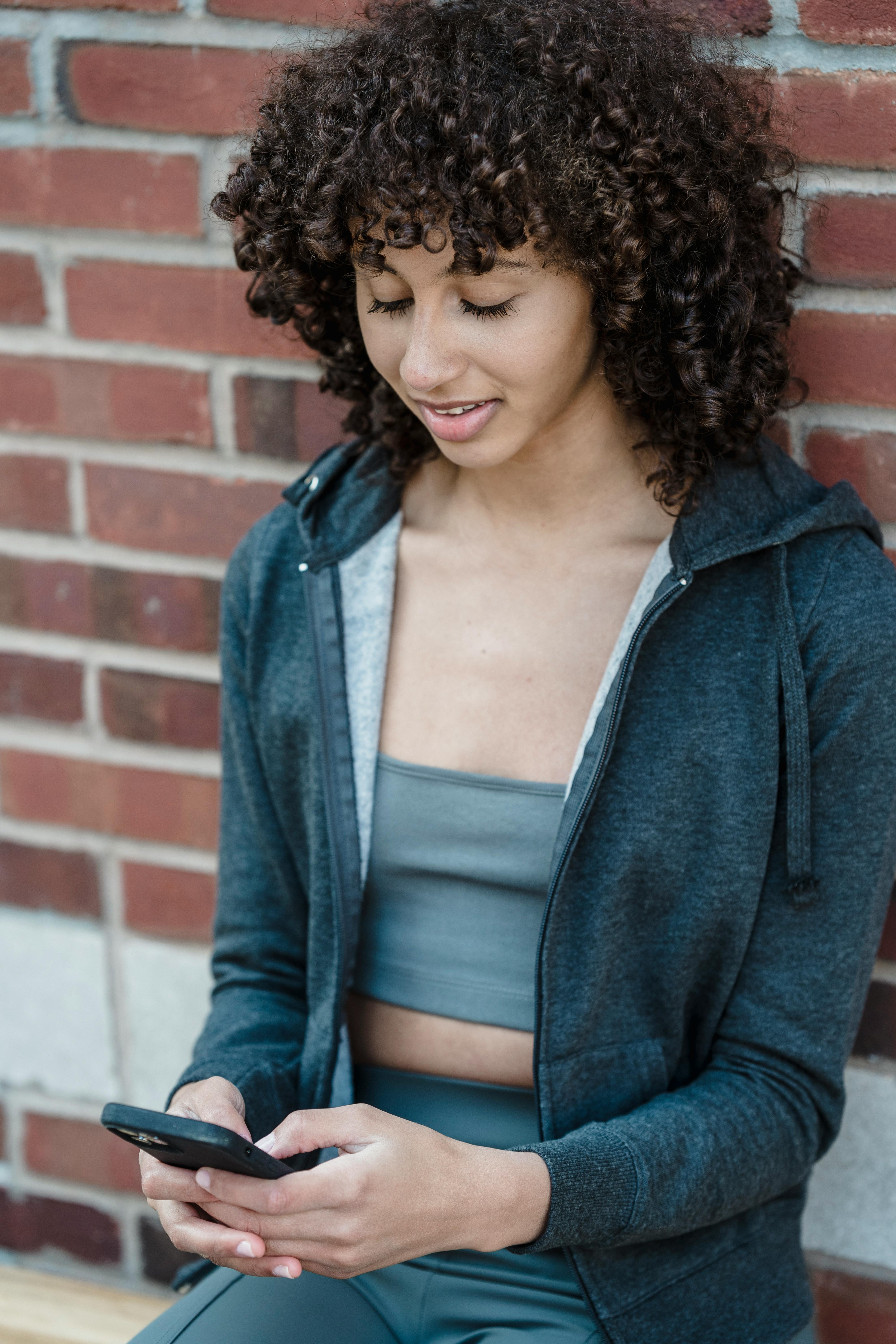 smiling young ethnic woman reading message on smartphone on street