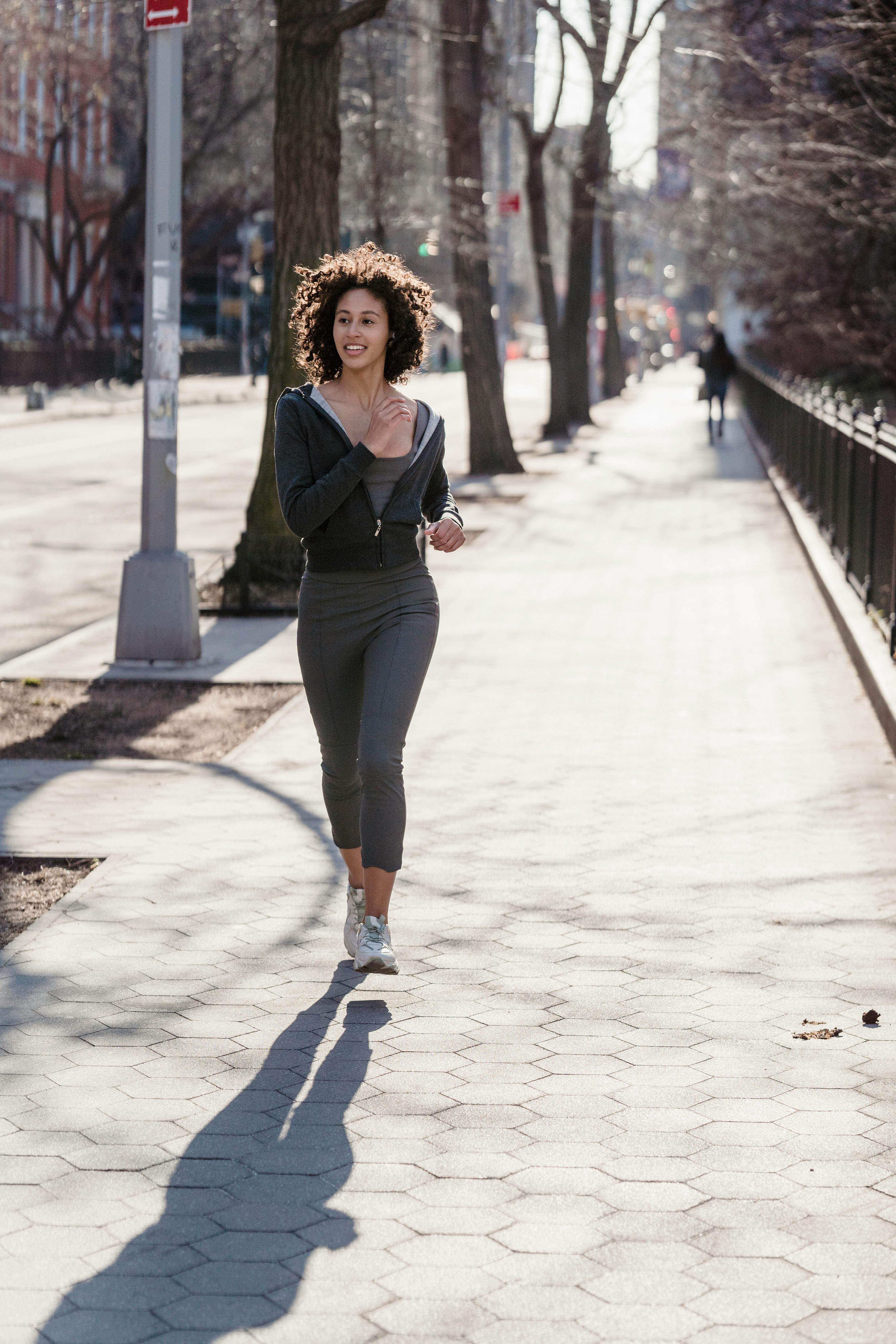 positive young ethnic sportswoman jogging on city street