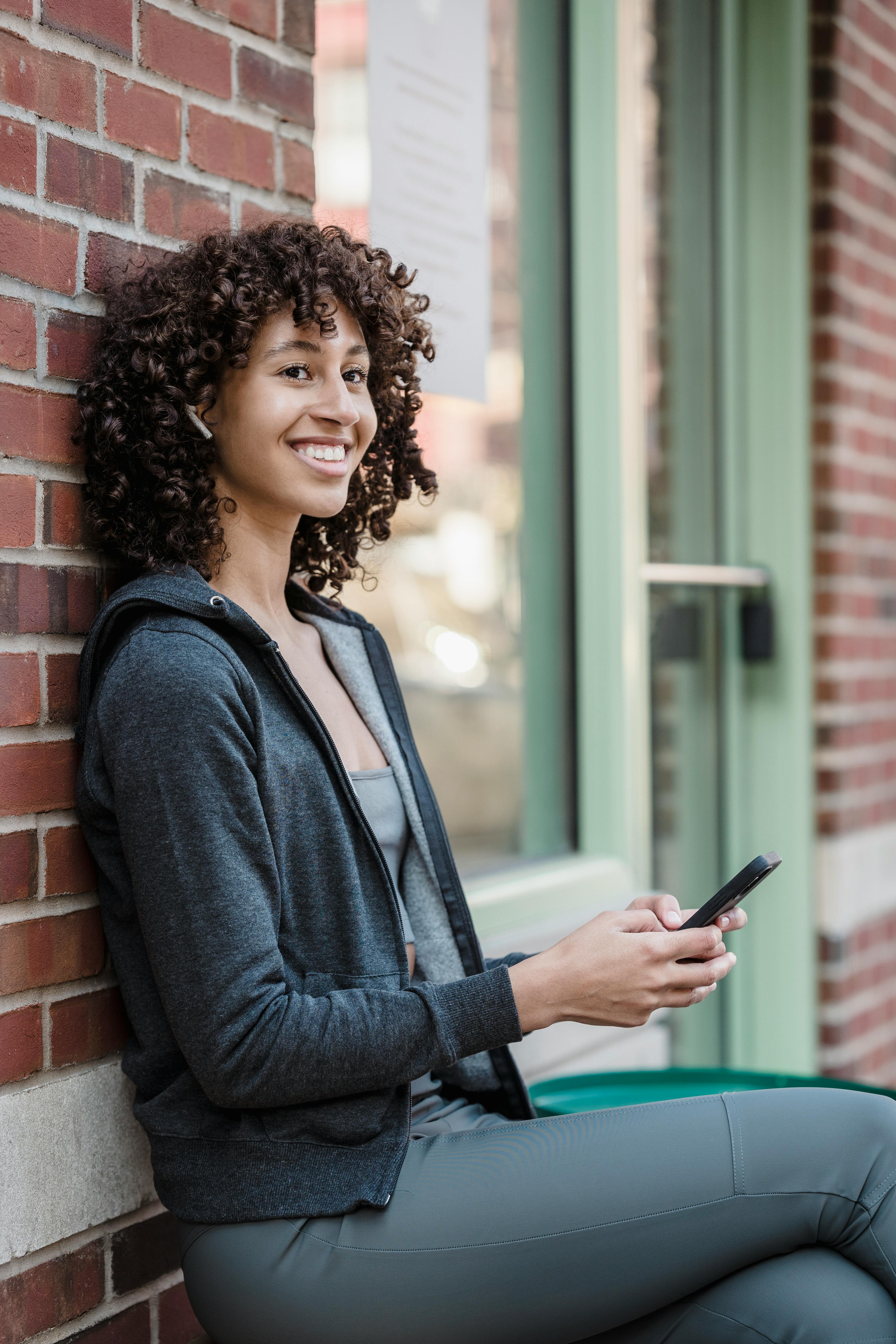 happy young ethnic woman having phone call via wireless earphones and smiling