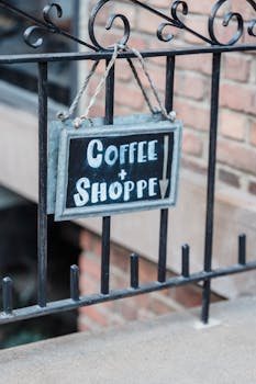 Rustic 'Coffee Shoppe' sign hanging on an iron fence outside a brick building, inviting customers.