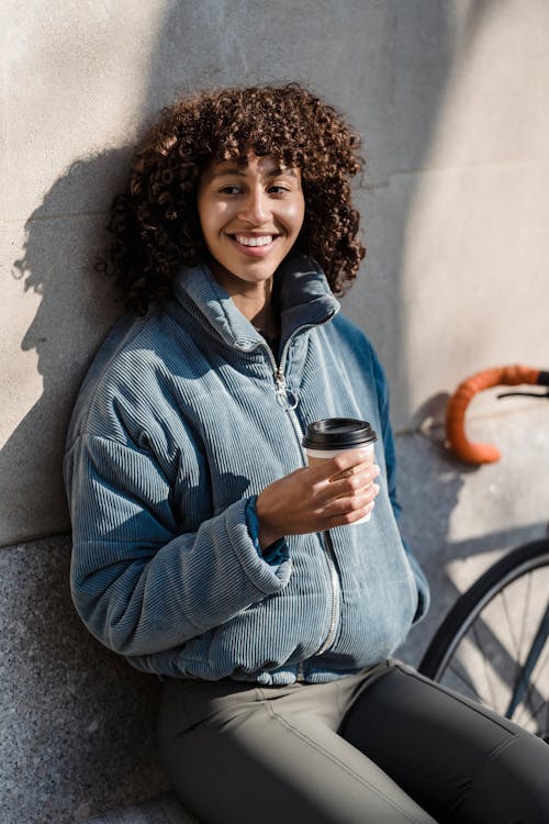 Free Cheerful ethnic woman with coffee to go on street Stock Photo