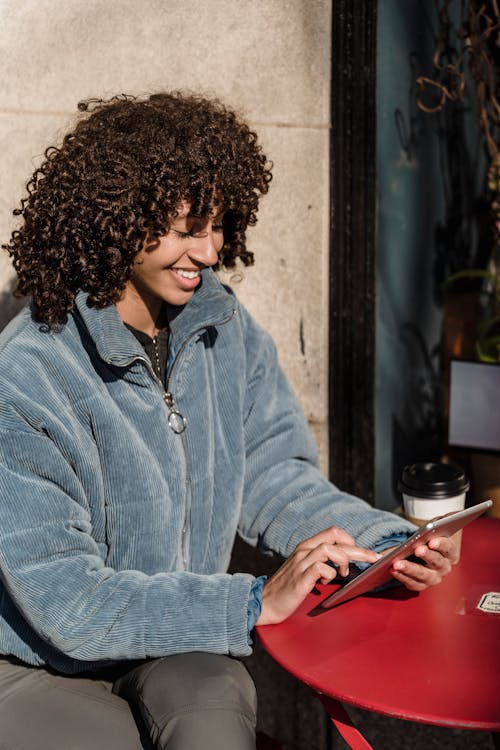 Cheerful ethnic woman touching screen on smartphone in urban cafeteria