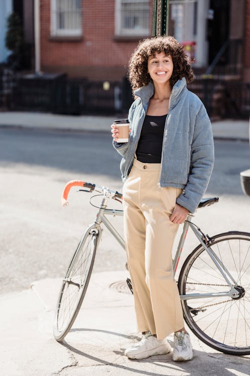 Free Delighted young ethnic female cyclist drinking takeaway beverage on street and smiling Stock Photo