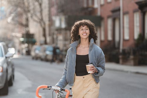 Cheerful young ethnic woman with and coffee in city