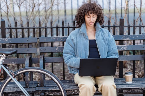 Concentrated ethnic female freelancer using netbook on bench in park