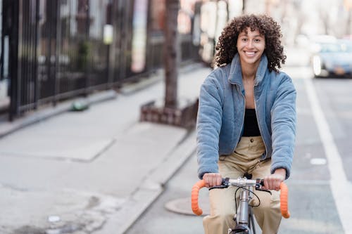 Joyful ethnic female teenager riding bicycle and smiling on street