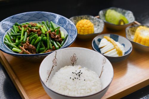 Free A vibrant Asian meal featuring rice, green beans, corn, and more on a wooden tray. Stock Photo
