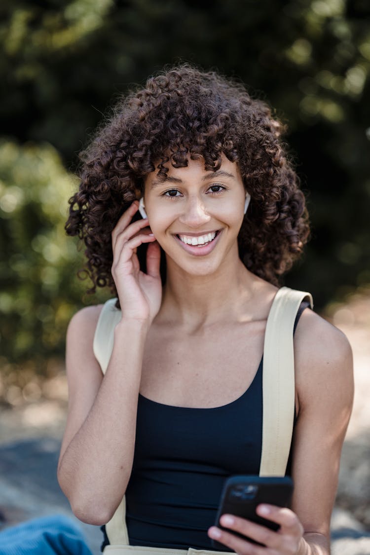 Smiling Ethnic Woman With Phone And Earphones In Park