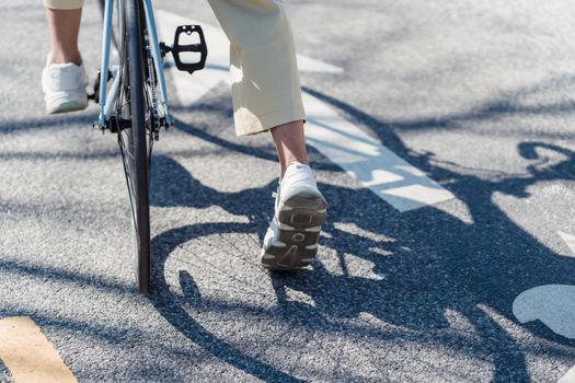 From above of crop anonymous person riding bicycle on asphalt road in sunny day