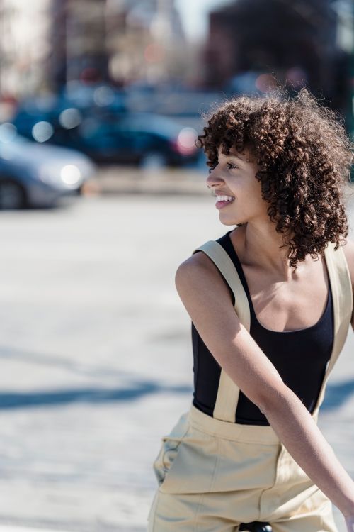 Free Smiling woman with curly hair enjoying a sunny day outdoors, wearing stylish casual attire. Stock Photo