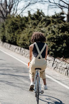 Back view of African American female riding bicycle on asphalt road along blurred trees