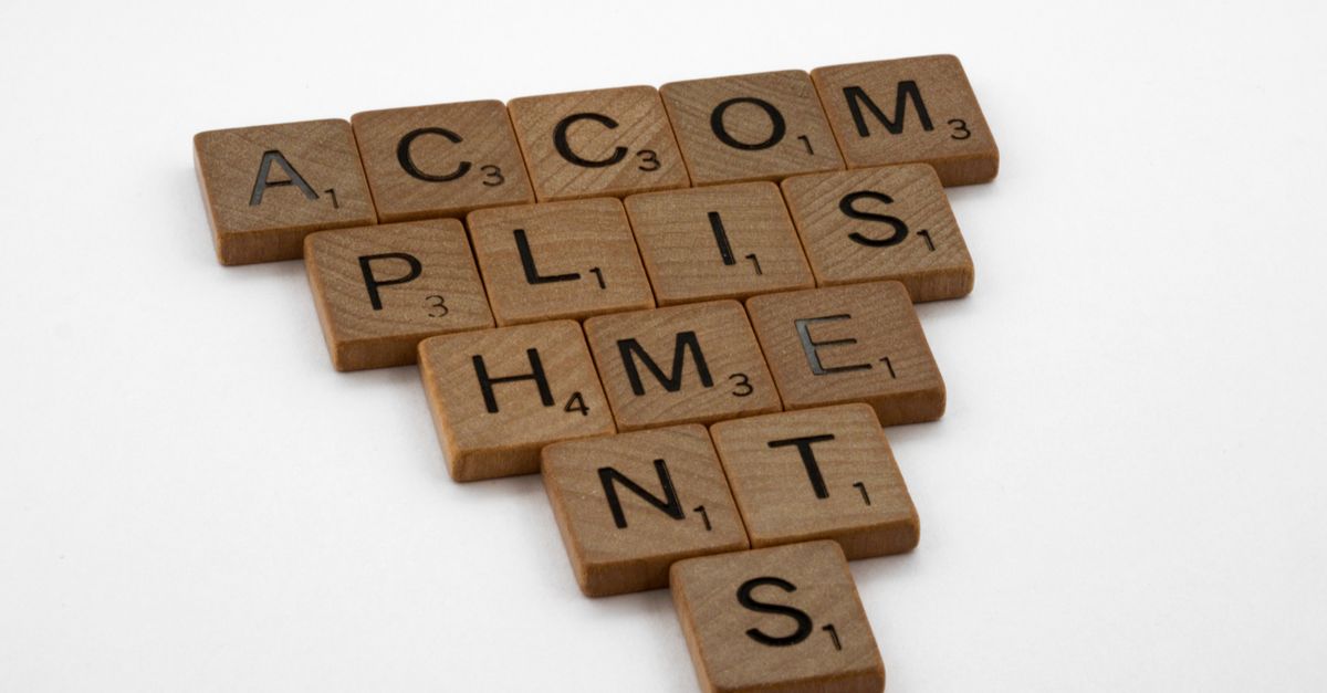 Wooden Scrabble tiles arranged to spell Accomplishments on a white background, ideal for success themes.