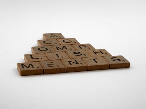 Wooden scrabble tiles forming the word 'accomplishments' on a white background.