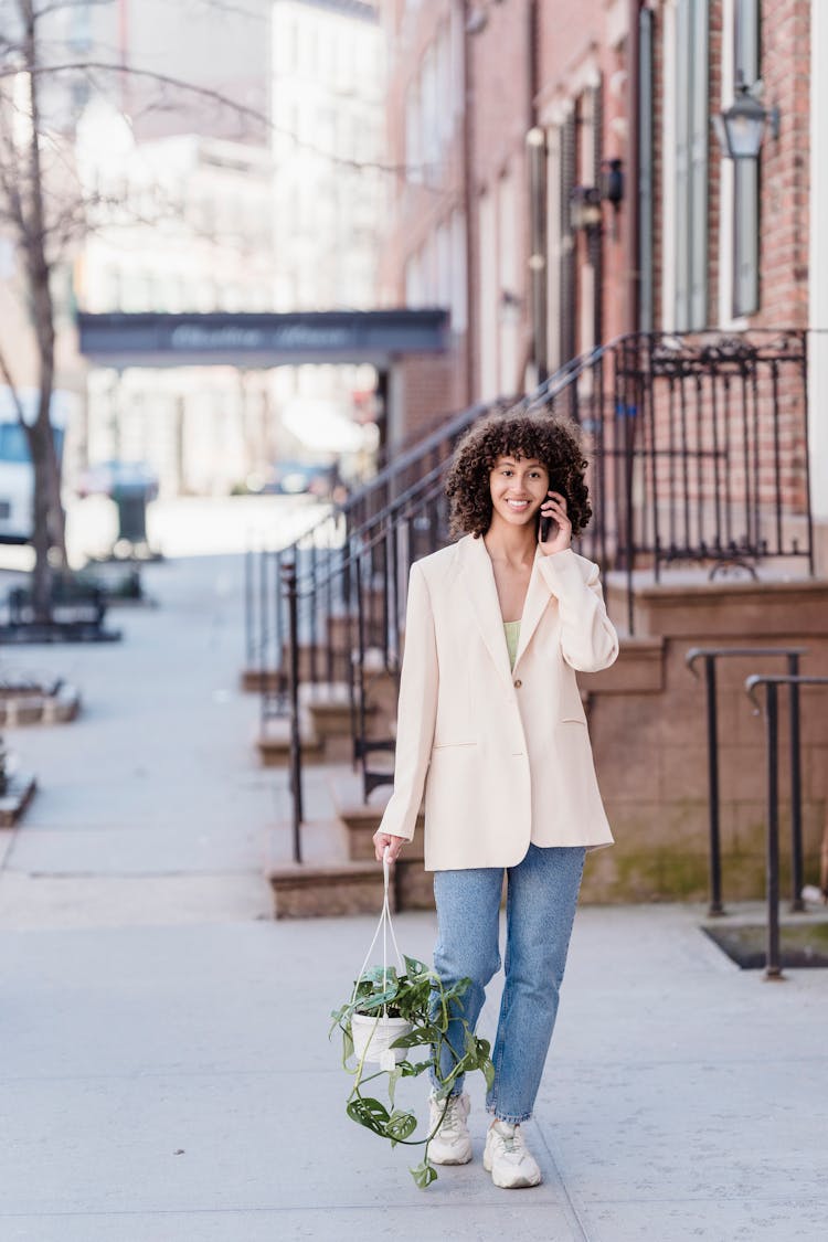 Black Female With Hanging Planter Walking Outside Having Phone Call