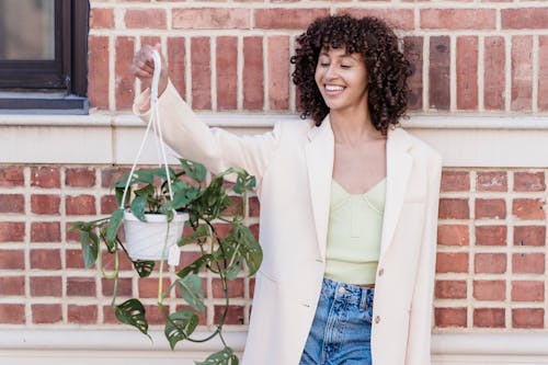 Happy black woman raising hanging planter against wall