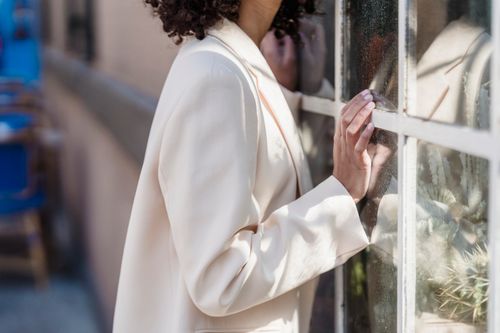 Free Side view of crop anonymous female with short dark curly hair near window of urban building on blurred background Stock Photo