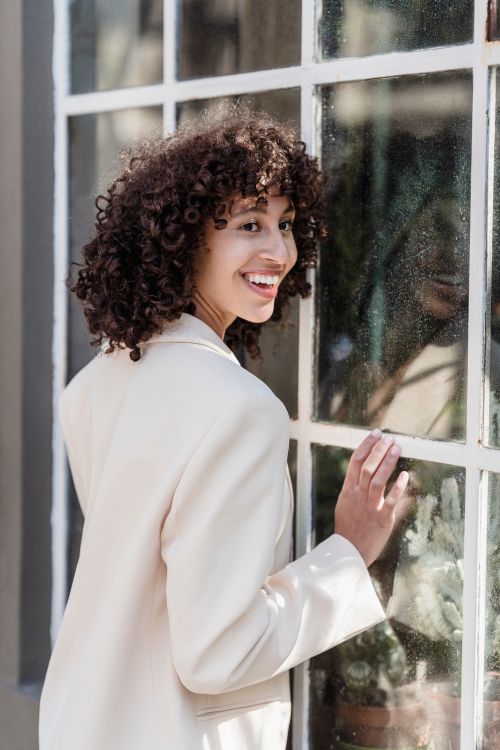 Free Positive ethnic female in elegant white jacket leaning on window of building on street in town Stock Photo
