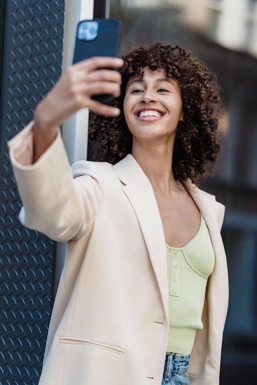 Happy ethnic woman taking selfie on smartphone in town