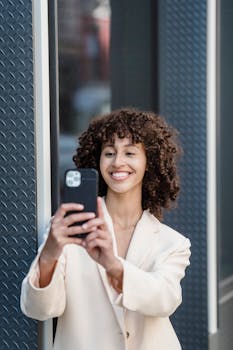 Content young ethnic female with curly hair taking self shot on mobile phone on street