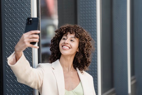 Satisfied ethnic woman taking selfie on smartphone in town