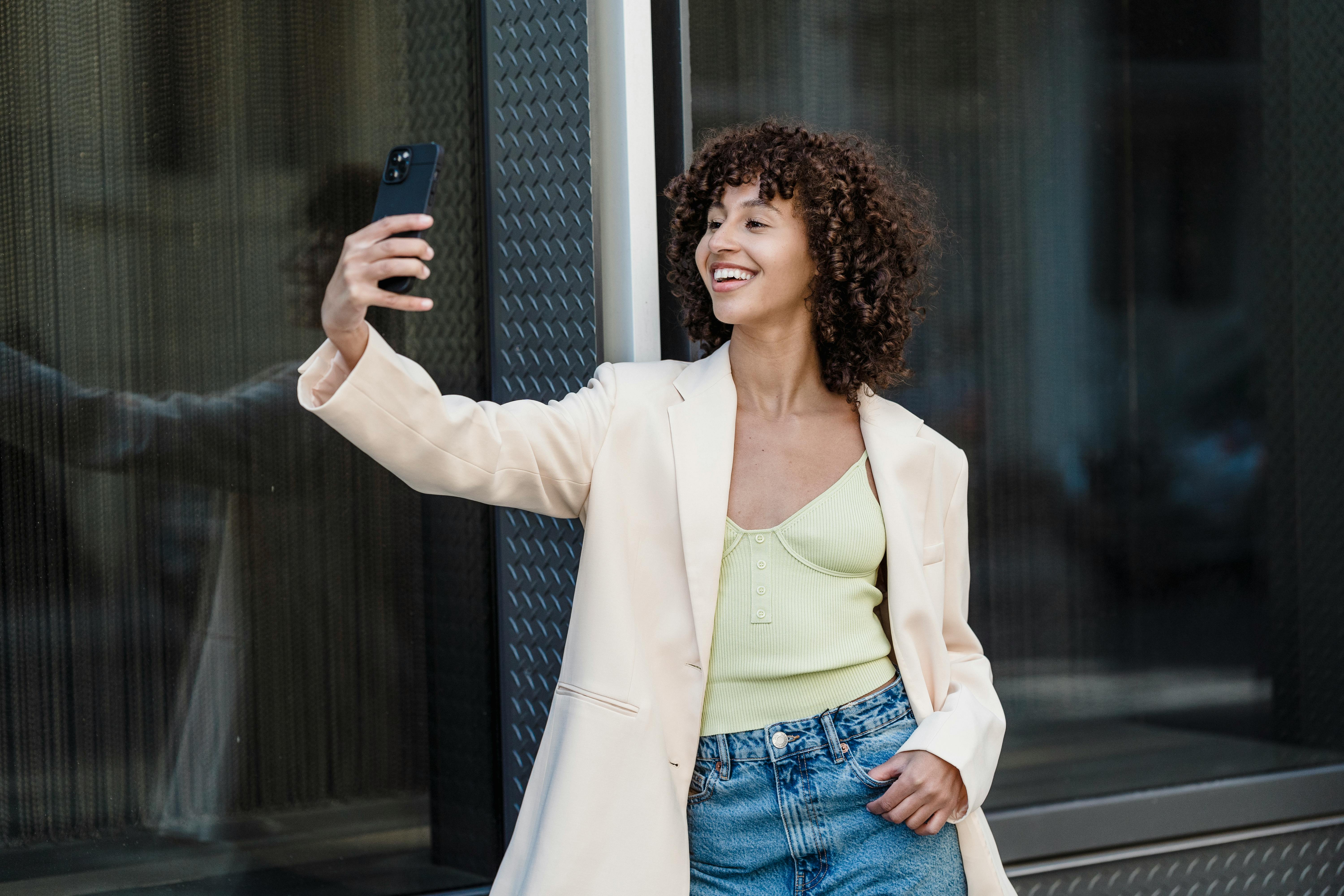 positive ethnic woman taking self portrait on smartphone in town