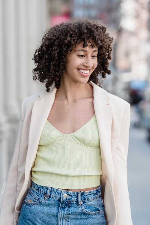 Free Cheerful young ethnic female in trendy wear with curly hair looking down on city street Stock Photo