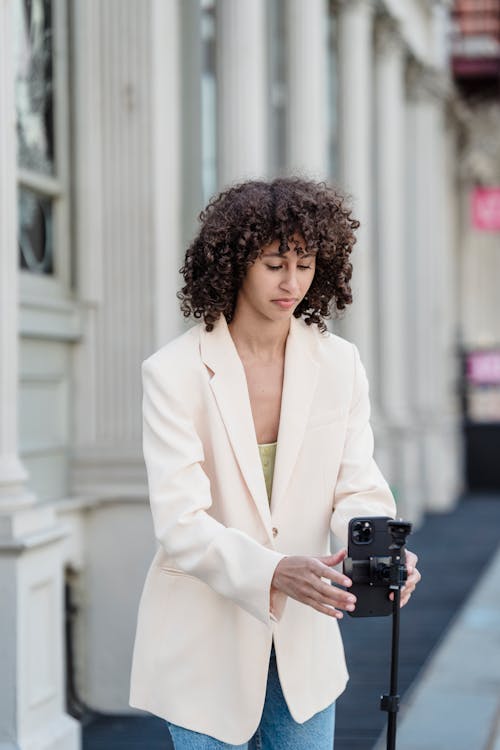 Free Focused young ethnic female vlogger in jacket preparing cellphone for video record on urban pavement in daytime Stock Photo