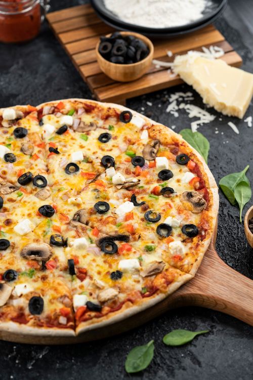 Free Delicious pizza topped with black olives, mushrooms, and cheese on a wooden tray, ready to serve. Stock Photo