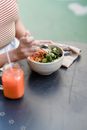 Crop anonymous female with bowl of yummy vegetarian salad and jar of smoothie at cafeteria table in daytime