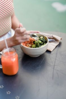 Crop anonymous female with bowl of yummy vegetarian salad and jar of smoothie at cafeteria table in daytime