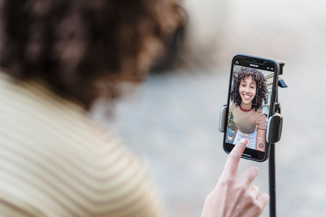 Free Crop cheerful young ethnic female vlogger touching screen on cellphone while preparing for video record in town Stock Photo