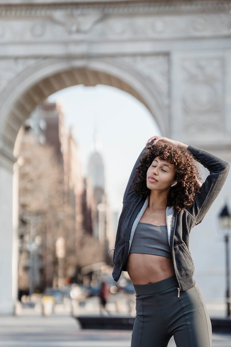 Peaceful Ethnic Sportswoman In Earbuds Warming Up Before Workout