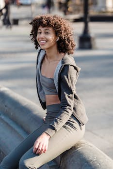 Smiling woman in activewear with curly hair enjoys a sunny day outdoors.
