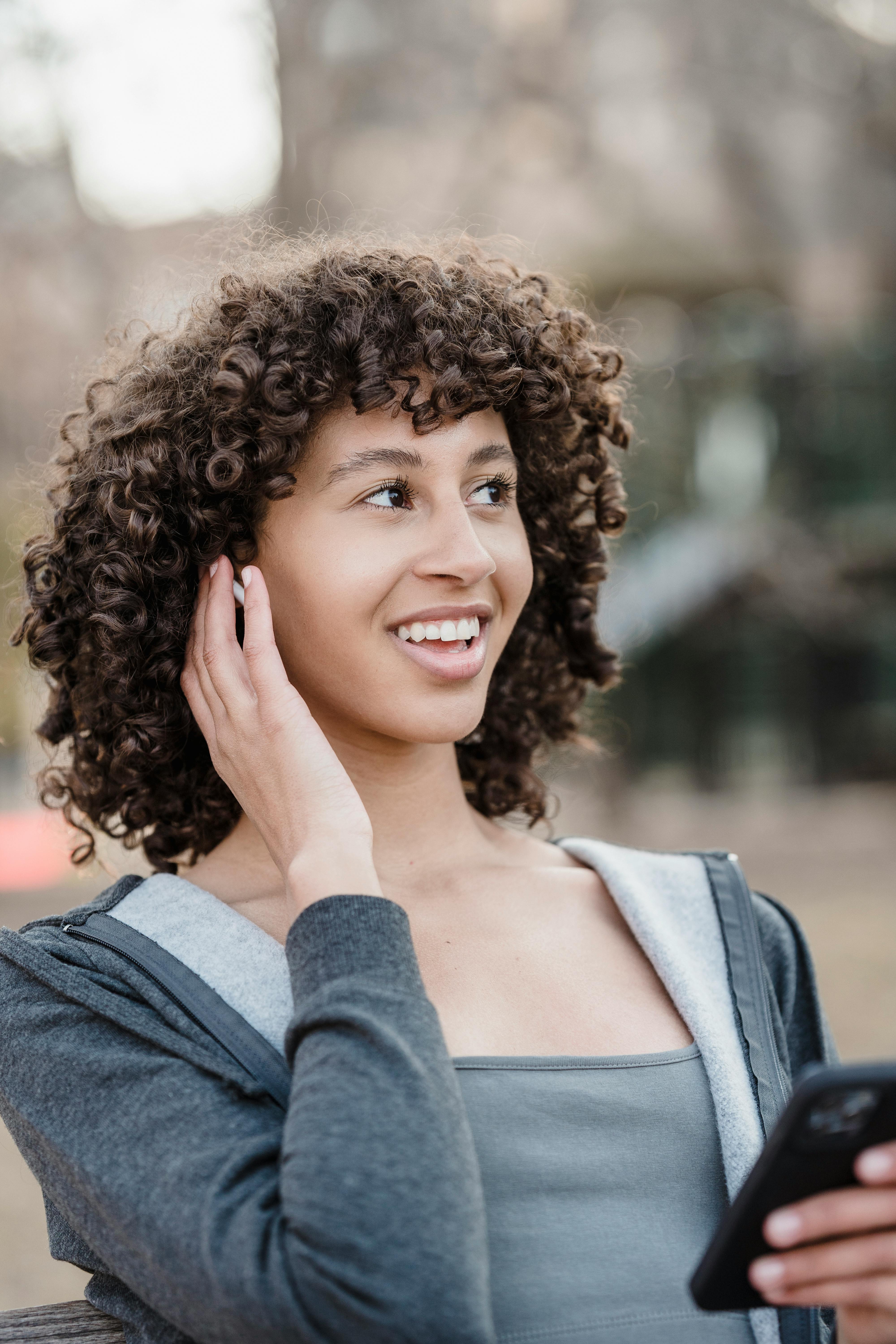 positive ethnic woman using smartphone and earbuds for phone call