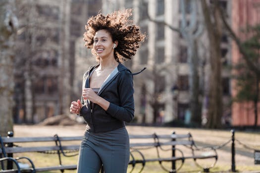 Positive ethnic female with flying curly hair listening to playlist in TWS earphones during running training in park