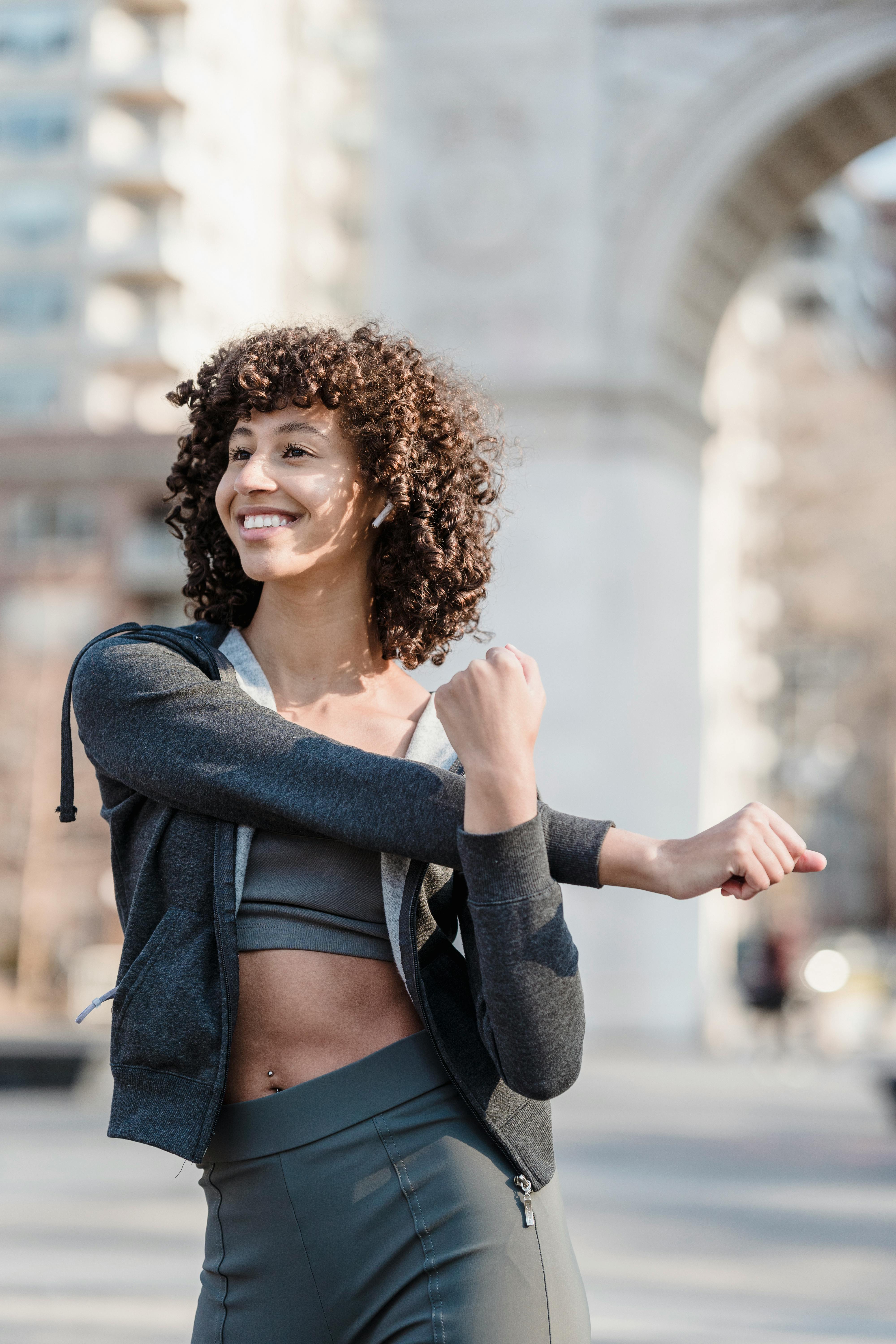 smiling fit ethnic woman in earbuds warming up before training