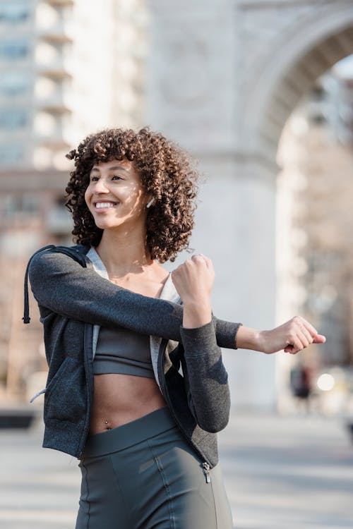 Free Smiling fit ethnic woman in earbuds warming up before training Stock Photo