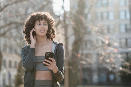 Free Ethnic sportswoman connecting earbuds with smartphone Stock Photo