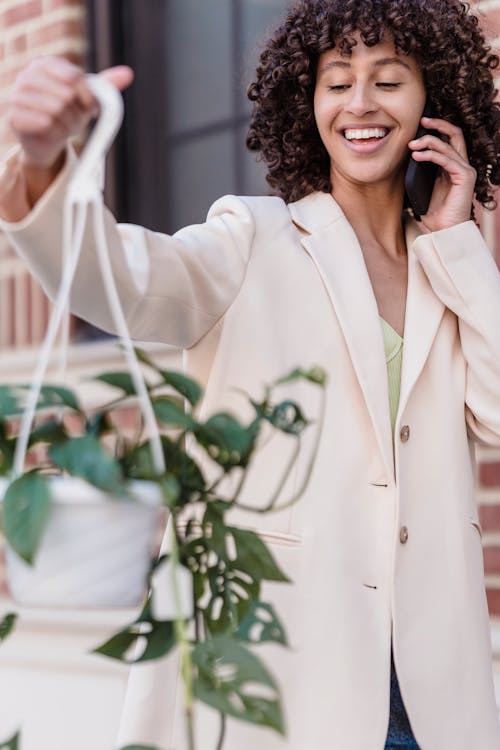 Cheerful ethnic woman talking on smartphone while standing with pot