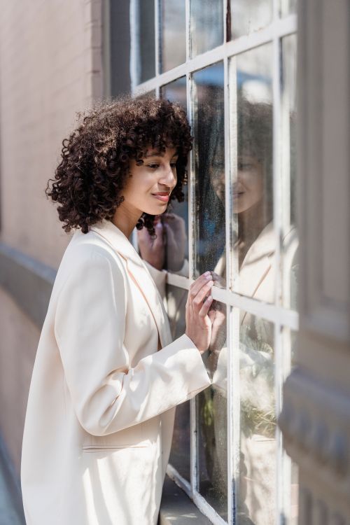 Free Side view of cheerful ethnic female with Afro curls standing near building with glass windows on sunny street in city Stock Photo
