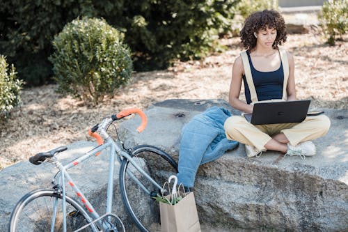 A Woman Using a Laptop on the Rock Formation Near the Bicycle